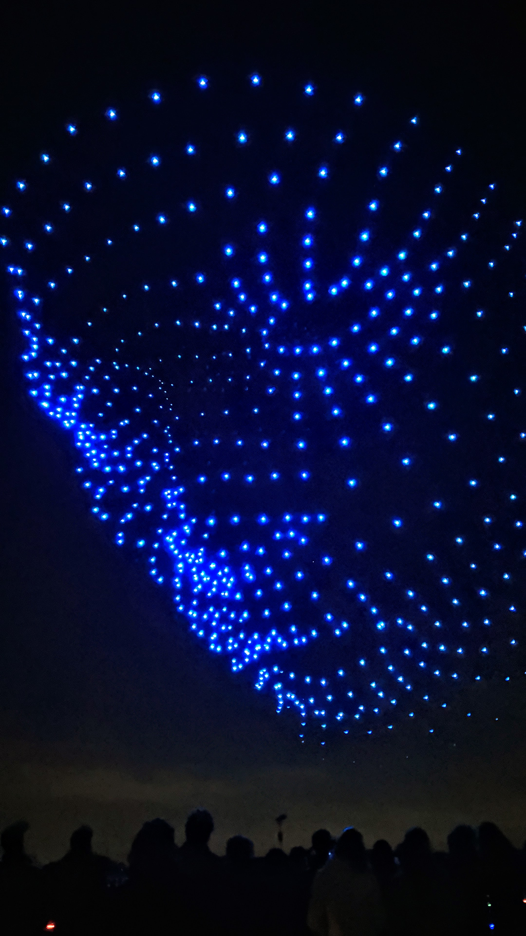 Nighttime drone light show forming a pattern in blue lights